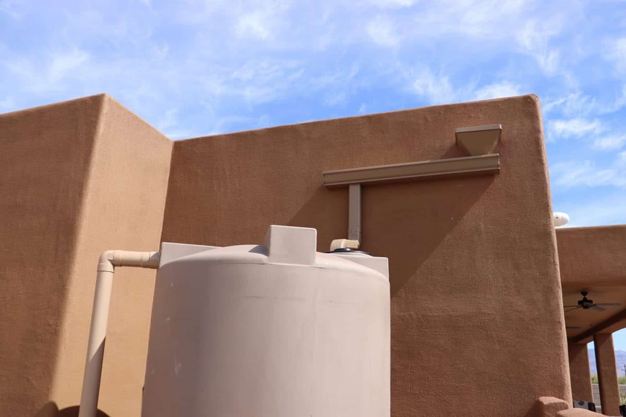 Completed residential rainwater harvesting system in Tucson, Arizona with roof scupper, downspout, and collection tank